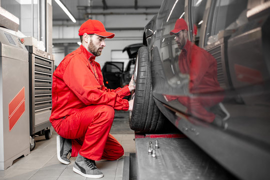 Two car service workers in red uniform changing wheel of a sport car at the tire mounting service