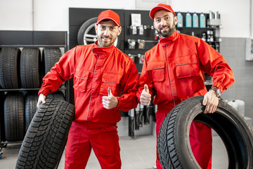 Portrait of a two car service workers in red uniform standing together with new tires at the store