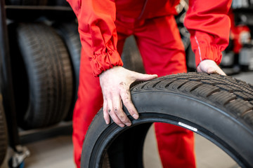 Worker in uniform carrying new tires at the car service or store, close-up view