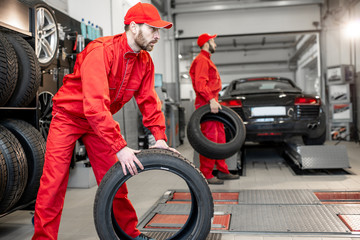 Car service workers in red uniform carrying new tires at the tire mounting service or shop