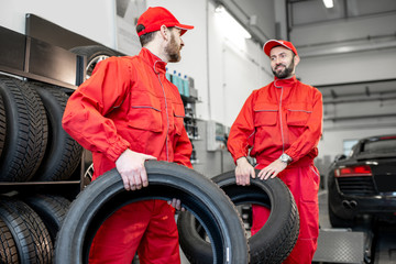 Car service workers in red uniform carrying new tires at the tire mounting service or shop