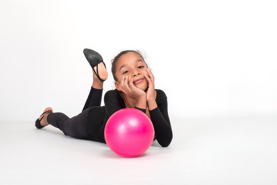 Studio shot of   attractive little  gymnast girl of wearing  black legends and a bathing suit with a pink ball on a white background, full length.