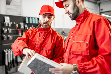 Auto mechanic in red uniform holding new and used air filter standing at the car service