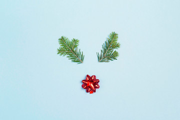 Fototapeta na wymiar Christmas deer face made of fir-tree branches and red bow on blue background. Flat lay, top view.