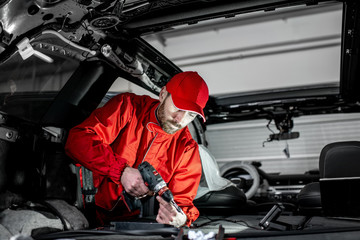 Handsome auto service worker in red uniform disassembling new car interior making some improvements