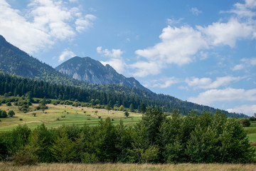 Beautiful mountain landscape in Romania with Piatra Craiului peak in the distance and grass covered hills.