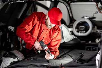 Handsome auto service worker in red uniform disassembling new car interior making some improvements