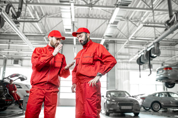Two auto mechanics in red uniform talking together during the break at the car service