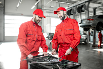 Portrait of a two handsome auto mechanics in red uniform standing with working tools at the car service © rh2010