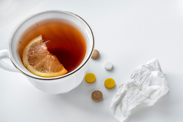 Tea with lemon, pills and handkerchief on the white table. The concept of colds.