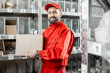 Handsome warehouse worker in red uniform taking some products from the shelves at the storage with...