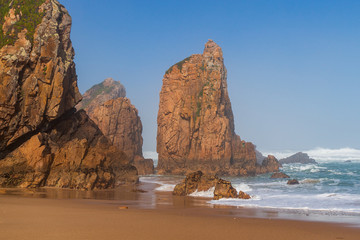 Pristine golden sand beach bordered by beautiful tall cliffs rising at the shore of the ocean. Ursa Beach seascape in Sintra, Portugal.