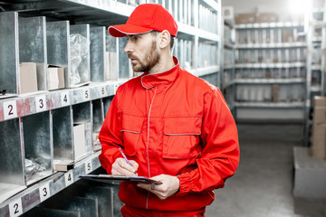 Warehouse worker in red uniform filling some documents checking goods at the storage