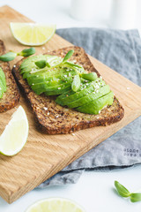 Two toasts with avocado on a wooden board on a breakfast table. The concept of vegetarian and healthy diet food.