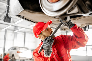 Auto mechanic in red uniform diagnosing car on the hoist at the car service
