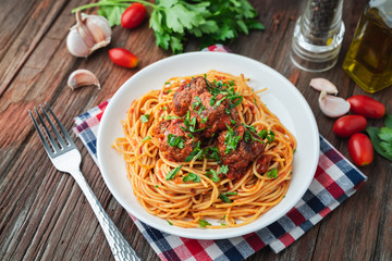 Spaghetti and meatballs with tomato sauce in white dish on wooden rustic board, Italian food closeup and top view.