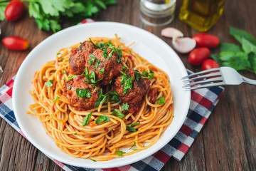 Spaghetti and meatballs with tomato sauce in white dish on wooden rustic board, Italian food closeup and top view.