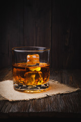 Whiskey with ice cube in a glasses on a rustic dark wooden table