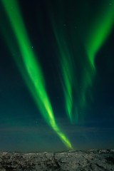 Fototapeta premium Beautiful stripes of the northern lights, aurora in the night sky above the hills.