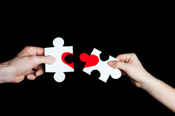 Puzzle with a red heart in the hands of a loving couple. Valentine's Day concept. Torn heart.On a black background