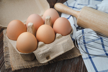 Eggs in carton with whisk and rolling pin on wooden table for cook and bakery concept