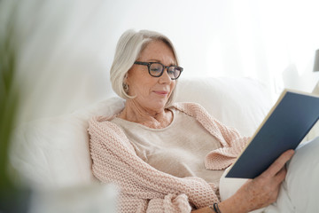 Beautiful senior woman relaxing in bed reading