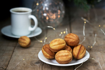 Homemade shortbread cookies in the shape of nuts on the background of a cup of coffee, fir branches and garlands.