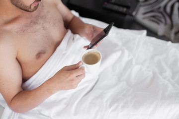Bearded man in bed drinking morning espresso coffee in sunrise light