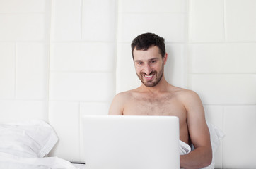 young man is working with laptop, lying on bed