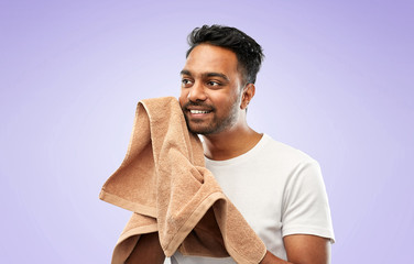 grooming, hygiene and people concept - smiling indian man with bath towel drying his face over ultra violet background