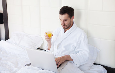 young man is working with laptop, lying on bed