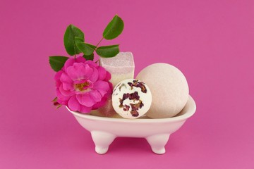 pink bath bombs set with rose extract. bath truffle, pink rose flower  in a white ceramic bath on a pink background. Organic Cosmetic Spa Body Kit