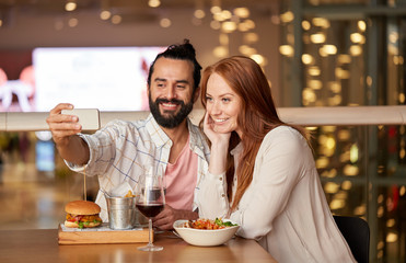 leisure, technology and people concept - happy couple having lunch and taking selfie by smartphone at restaurant