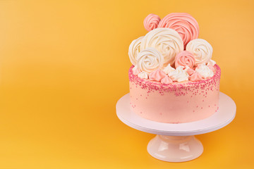 Birthday pink cake, decorated with meringue cookies on a yellow background.