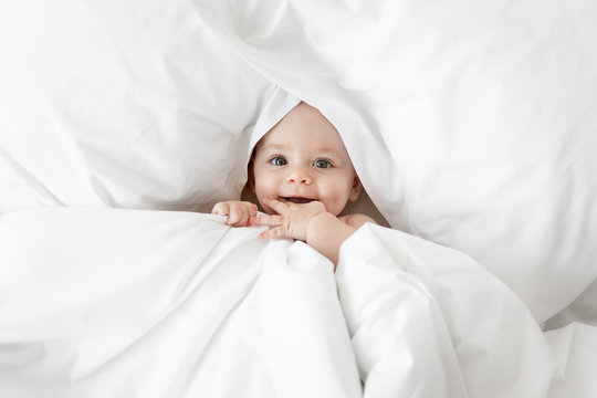 Cute baby peeking from white sheets