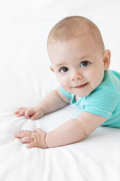 Portrait of cute baby lying on tummy on white bed