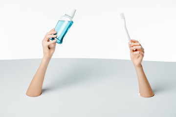 cropped shot of woman holding toothbrush and mouthwash through holes on white
