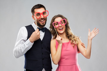 photo booth, fun and people concept - happy couple posing with party props over grey background