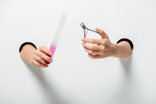 Cropped Image Of Woman Holding Nail Scissors And Nail File For Manicure In Holes On White