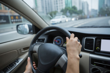Hands holding steering wheel while driving car on city road