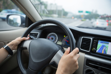 Hands holding steering wheel while driving car on city road
