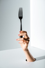 cropped image of woman holding fork in hand through hole on white