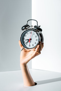 cropped image of woman holding retro styled alarm clock in hand through hole on white