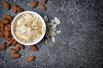 Top view of almond slices and whole nut in white bowl as ingredient for confectionery
