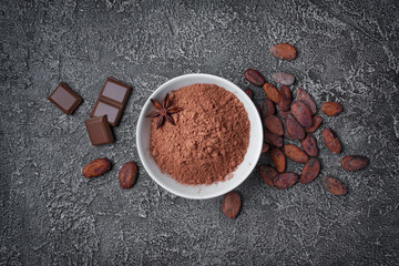 .Top view of cocoa powder in white bowl with pieces of chocolate bar and cocoa beans