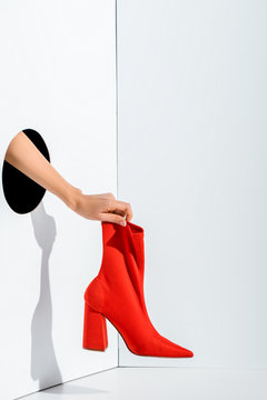 cropped image of girl holding red stylish high heel in hand through hole on white