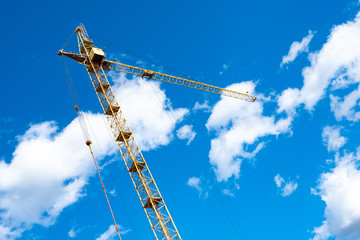 against the background of the blue sky and clouds is a tower crane tilted