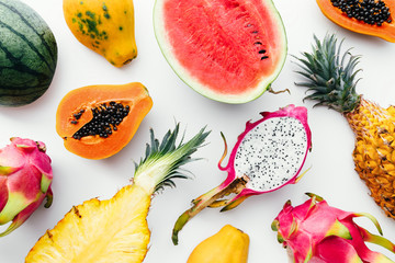 Flat lay tropical fruit layout made of dragon fruit, watermelon, papaya and pineapple on a white background, creative summer food concept