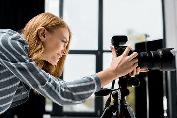 side view of smiling young female photographer working with professional photo camera in studio