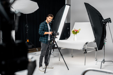 handsome young photographer working with camera and lighting equipment in photo studio
